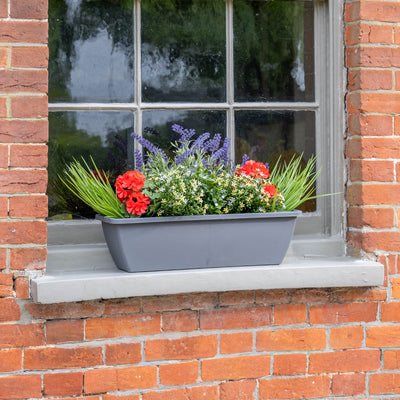 Window box with red, purple and yellow flowers with some grass greenery on a brick wall