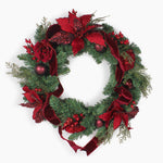 A festive Christmas wreath decorated with green pine branches, red glitter poinsettias, red velvet ribbons, red berries, and dark red ornaments, shown against a plain white background.