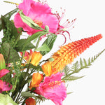 A close-up of a mixed floral arrangement featuring bright pink flowers, orange and yellow blossoms, green leaves, and fern-like foliage on a plain white background.
