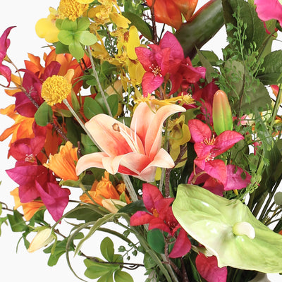 A vibrant artificial flower arrangement featuring a bright pink, orange and yellow flowers, and green foliage on a white background.