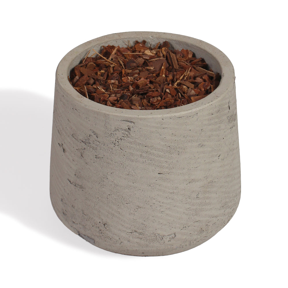 A small cylindrical concrete planter pot filled with brown wood chips or bark, photographed on a clean white background.
