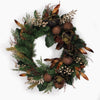 An artificial holiday wreath featuring green pine branches, dark green magnolia leaves, bronze-brown pinecones, gold-toned accents, and small gold berry clusters, photographed against a plain white background.