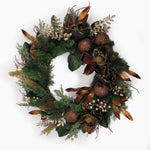 An artificial holiday wreath featuring green pine branches, dark green magnolia leaves, bronze-brown pinecones, gold-toned accents, and small gold berry clusters, photographed against a plain white background.