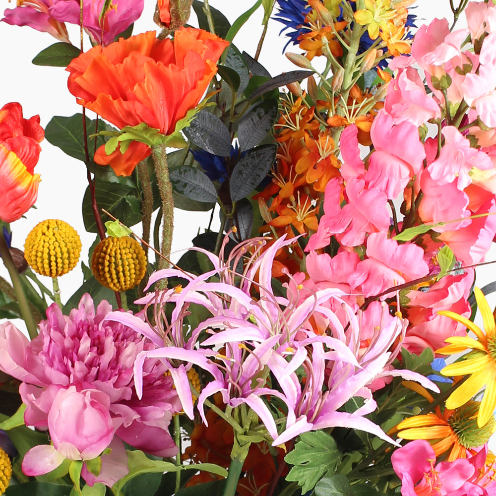 A dense, vibrant artificial flower arrangement featuring pink, orange and yellow flowers and green foliage on a white background.