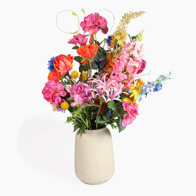 A vibrant artificial flower arrangement in a textured beige ceramic vase, set against a plain white background.