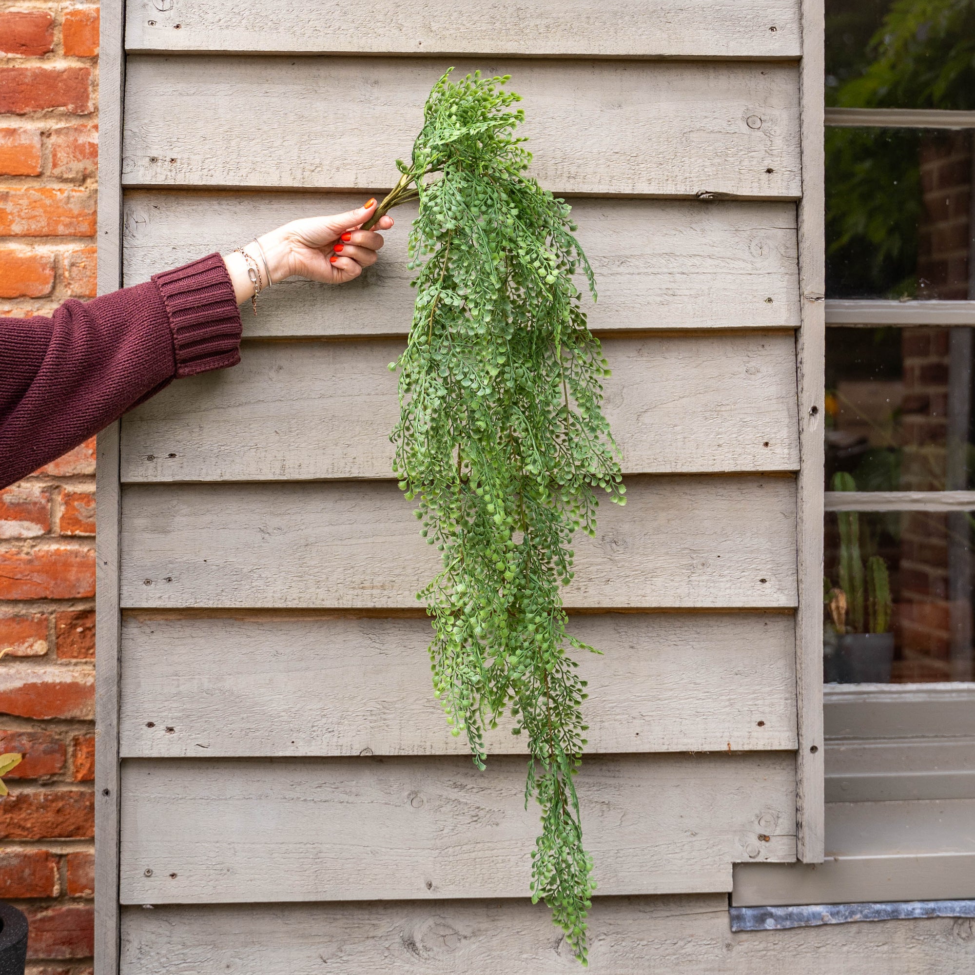 Person hanging a green plant on a wooden wall next to a brick wall.