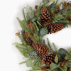 A close up of a festive artificial Christmas wreath made of green pine branches, decorated with large brown pinecones, small orange-brown pinecones, and round green eucalyptus leaves, photographed on a clean white background.
