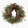 A festive pine wreath decorated with green pine needles, brown pinecones, eucalyptus leaves, and a large brown velvet bow, photographed against a clean white background.