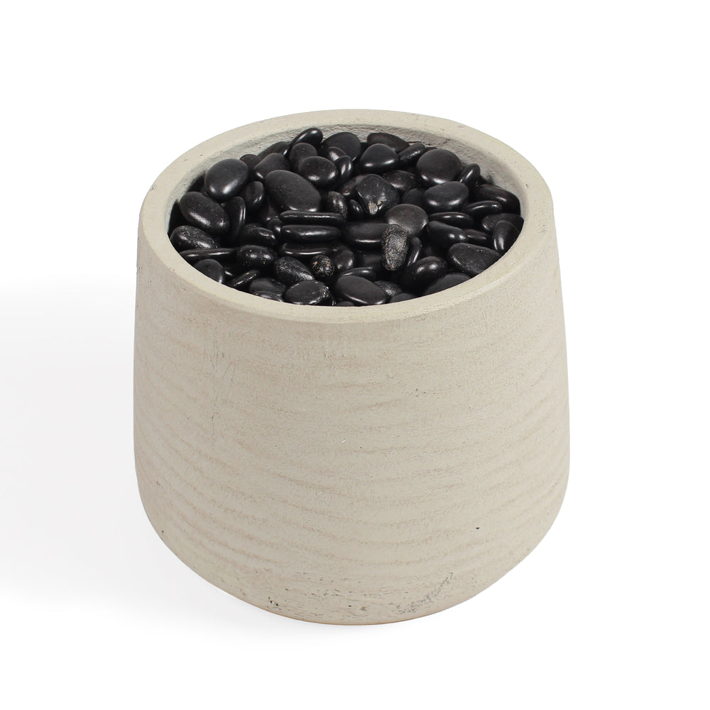 A cylindrical fibreclay pot filled with smooth black decorative stones, shown on a clean white background.