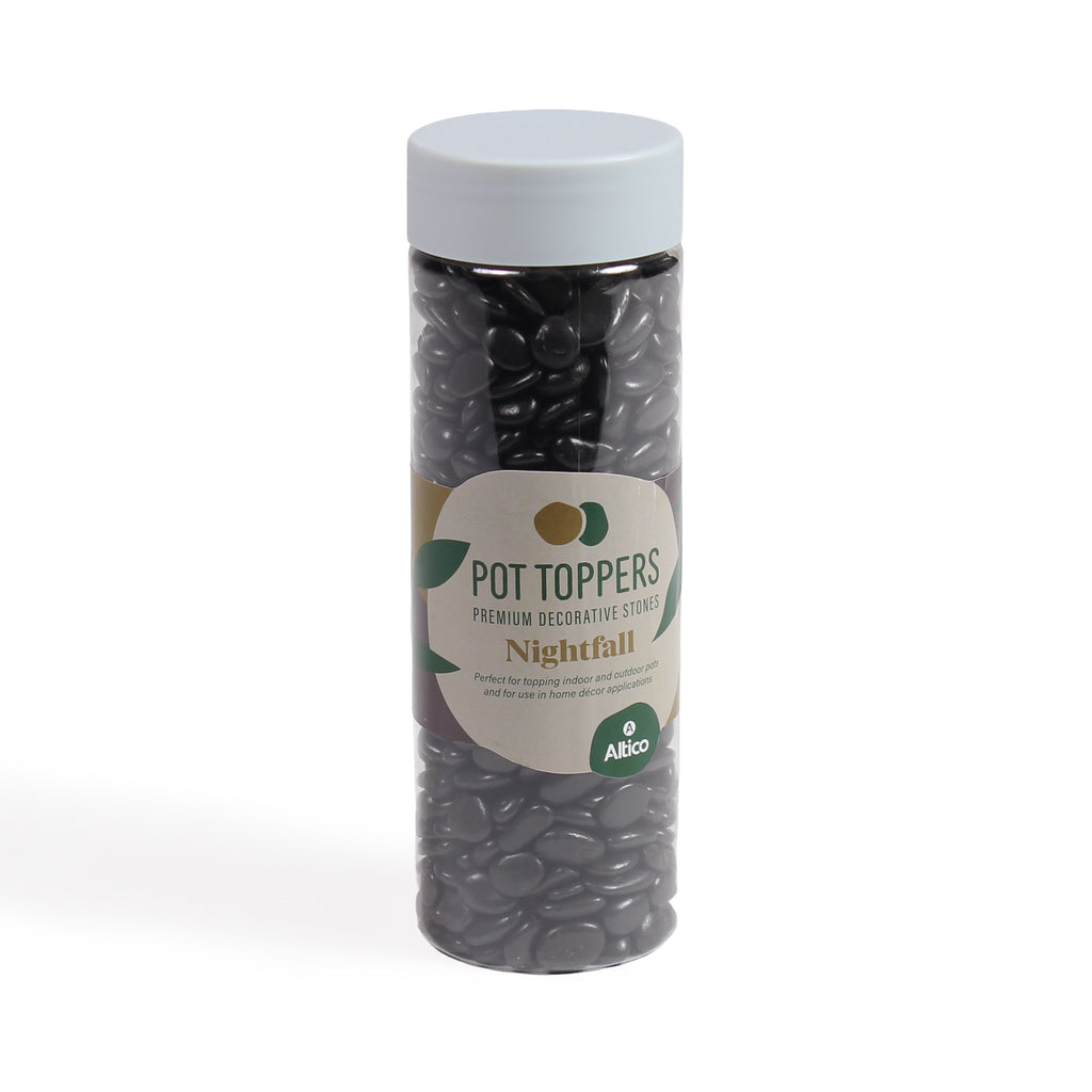 A tall, clear plastic jar filled with glossy black decorative stones, featuring a white lid and a cream and green colored label.