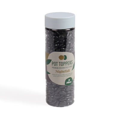 A tall, clear plastic jar filled with glossy black decorative stones, featuring a white lid and a cream and green colored label.