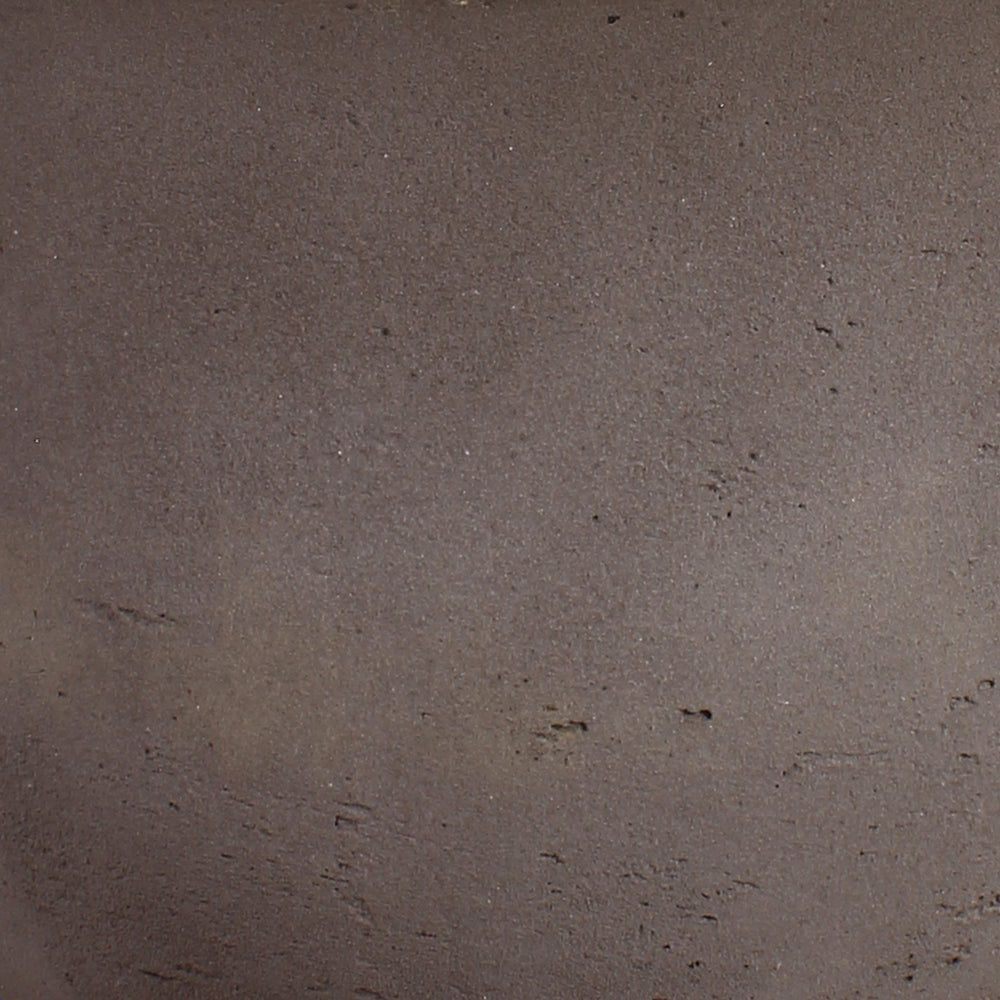 A close-up texture shot of a dark brown, matte, and slightly granular material surface.