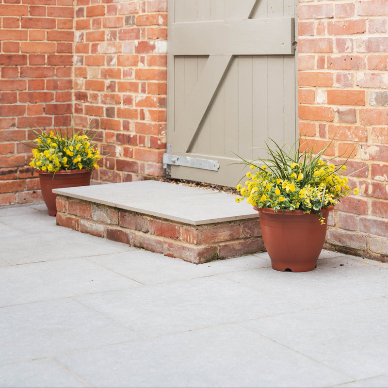 Brick wall with a closed wooden gate and potted yellow flowers on a patio.