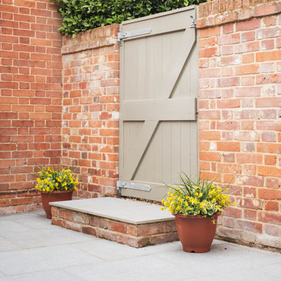 Brick wall with a closed wooden gate and two potted plants.