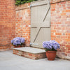 Brick wall with a closed gate and two potted flowers on a patio.