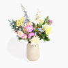 A vibrant artificial flower bouquet in a textured beige ceramic vase, set against a clean white background.