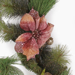 A close up of a glittery pine garland with blush pink poinsettias and gold ornaments on a white background.