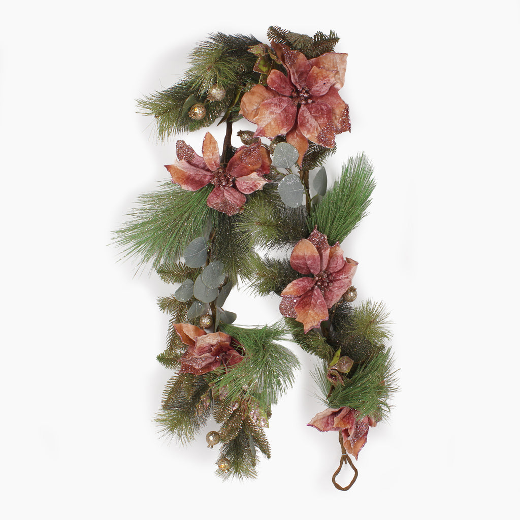 A Christmas garland featuring glittery  green pine needles, silver eucalyptus leaves, and dusty pink poinsettia flowers with small gold pinecones, shown against a plain white background.