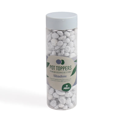 A clear plastic jar of light grey premium decorative stones, featuring a light gray lid and a beige label with green accents, set against a plain white background.