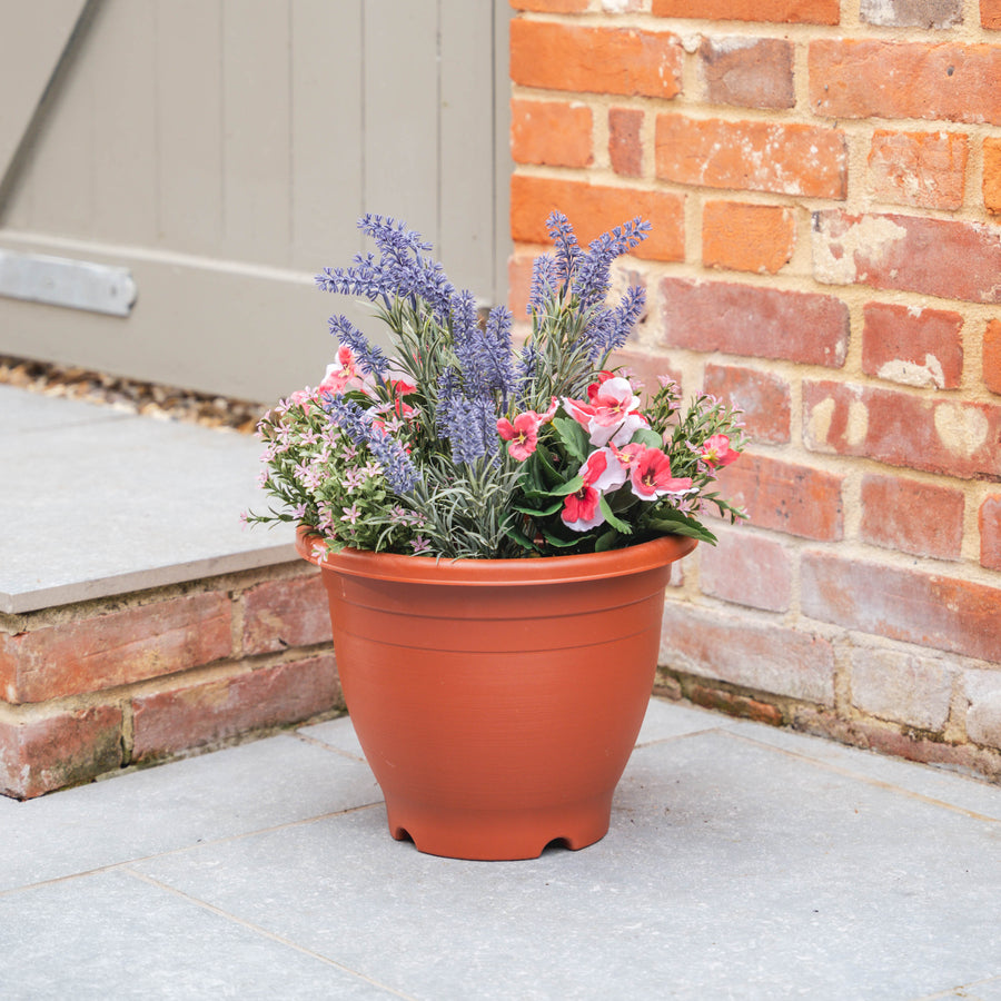Plastic pot with colourful flowers on a patio next to a brick wall