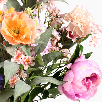 A close-up of a floral arrangement featuring large peach and pink blossoms with sage green leaves on a white background.