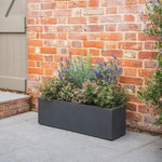 Tall rectangular planter with colourful flowers against a brick wall