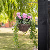 Pink flowers and foliage in a basket, hanging on a bracket in a garden