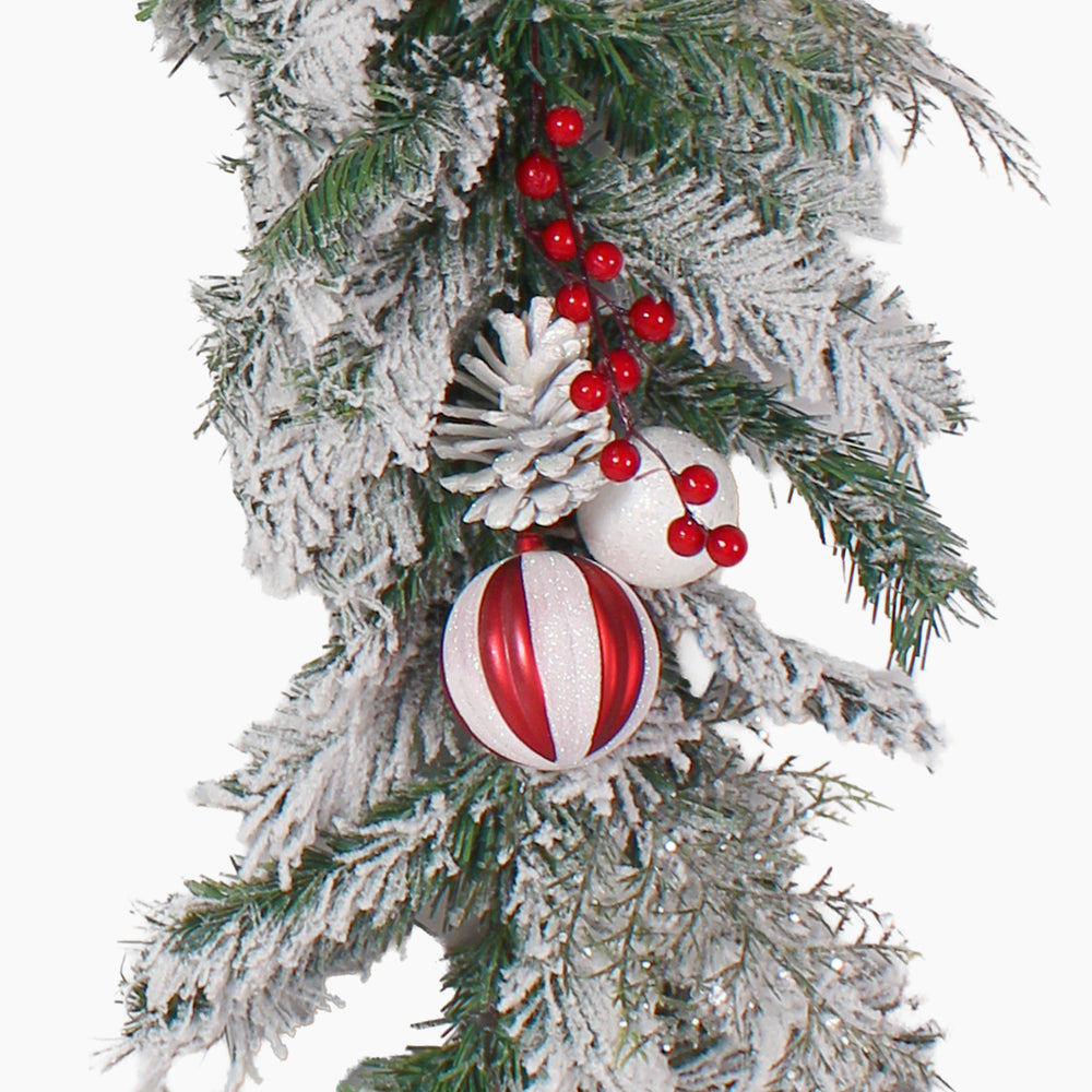 A festive Christmas garland branch decoration featuring a white pinecone, red and white ornaments with and clusters of red berries, isolated on a white background.