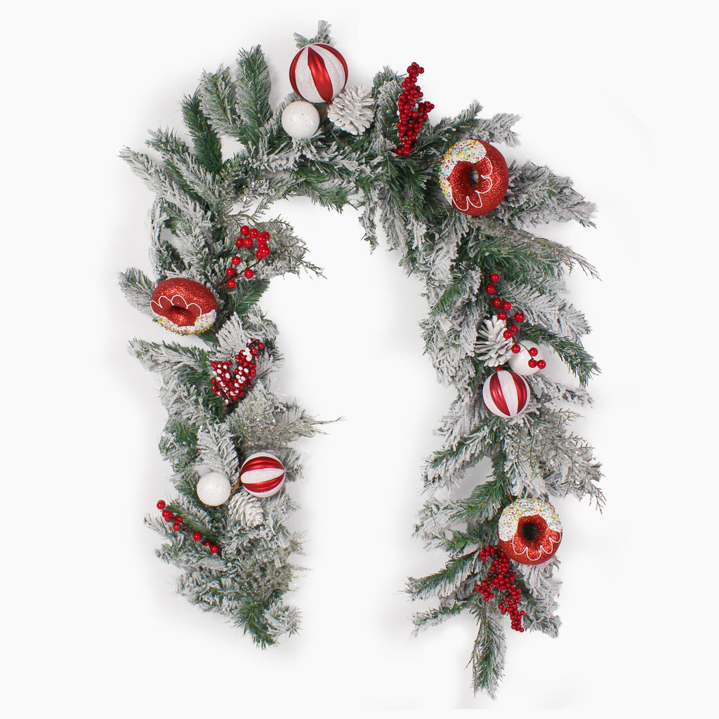 A festive Christmas wreath decorated with frosted green pine branches, red berries, red-and-white striped ornaments, white baubles, and donut ornaments, shown on a plain white background.