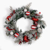 A festive Christmas wreath with frosted green pine branches, red berries, and red and white striped doughnut ornaments, photographed against a plain white background.