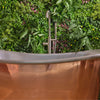 Copper bathtub with a modern faucet against a green foliage background