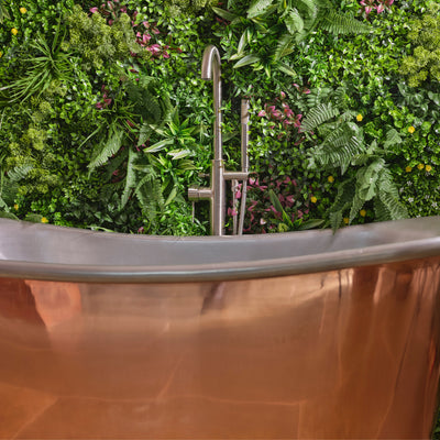 Copper bathtub with a modern faucet against a green foliage background