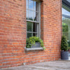 Brick building with a window box and potted plants on a wooden deck.
