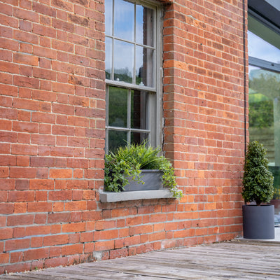 Brick building with a window box and potted plants on a wooden deck.