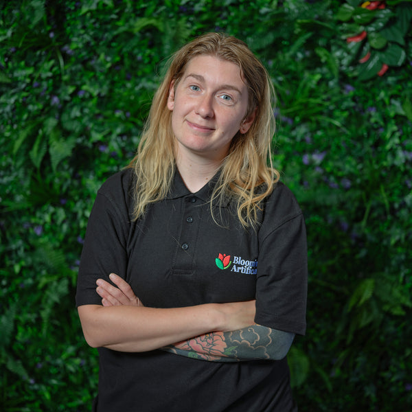 Person wearing a black shirt with a logo against a green leafy background
