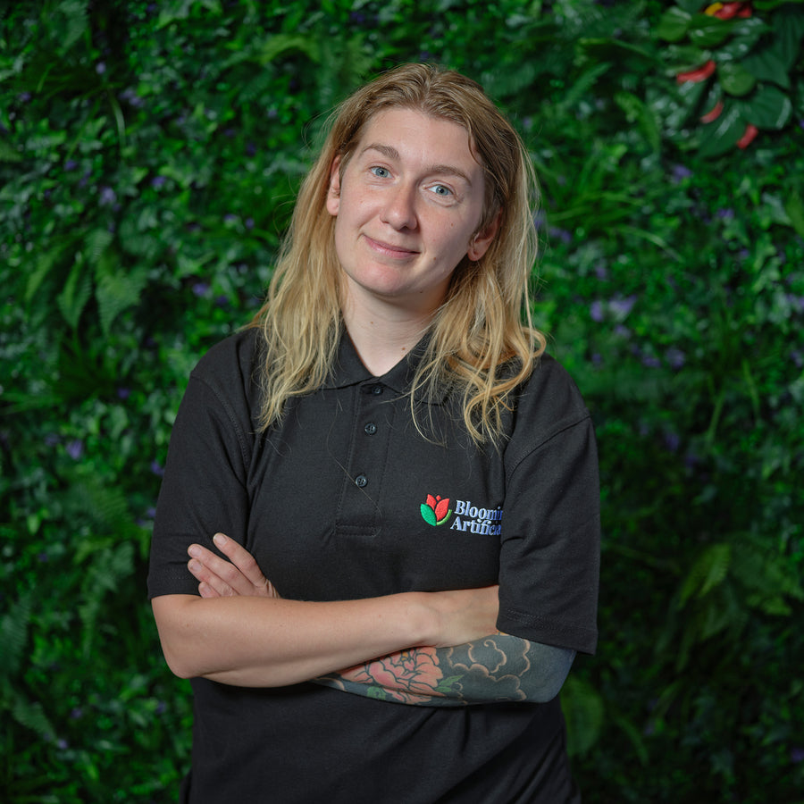 Person wearing a black shirt with a logo against a green leafy background