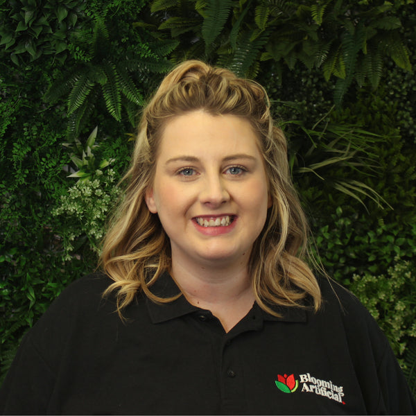 Person wearing a black shirt with a logo against a green leafy background