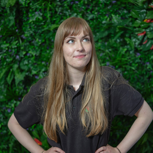 Woman in a black shirt standing against a green leafy background