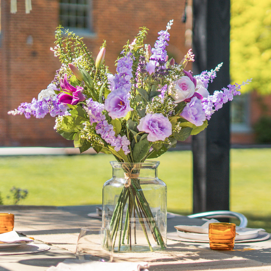 Bouquet of purple and pink flowers in a clear vase on a table outdoors.