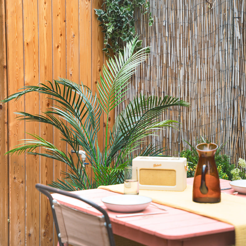 Outdoor setting with a table, chairs, and plants against a wooden and bamboo wall.