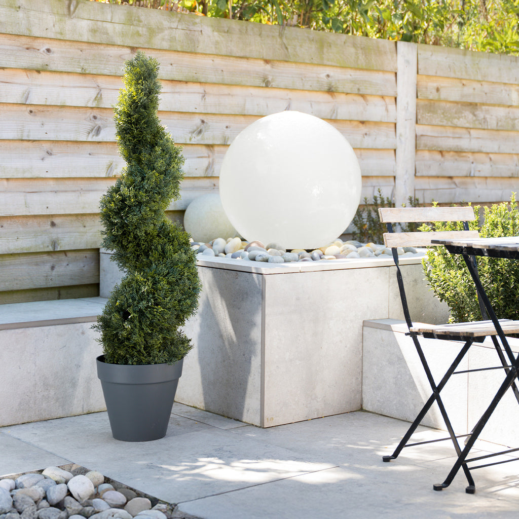 Garden setting with a potted cedar spiral, spherical water feature, and outdoor furniture.