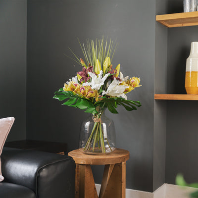 Bouquet of flowers in a clear vase on a wooden side table against a dark gray wall.