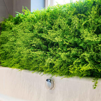 Artificial green wall panels surrounding a white bathtub.