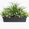 Artificial greenery arrangement in a black container on a white background