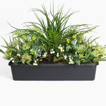 Artificial greenery arrangement in a black container on a white background