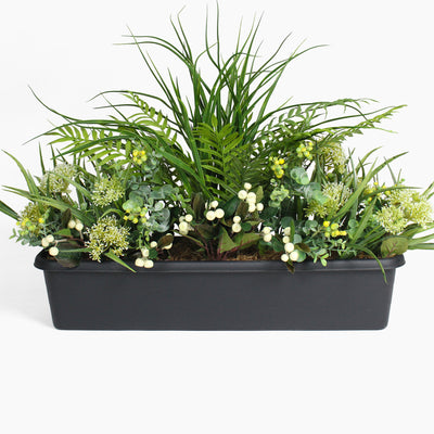 Artificial greenery arrangement in a black container on a white background