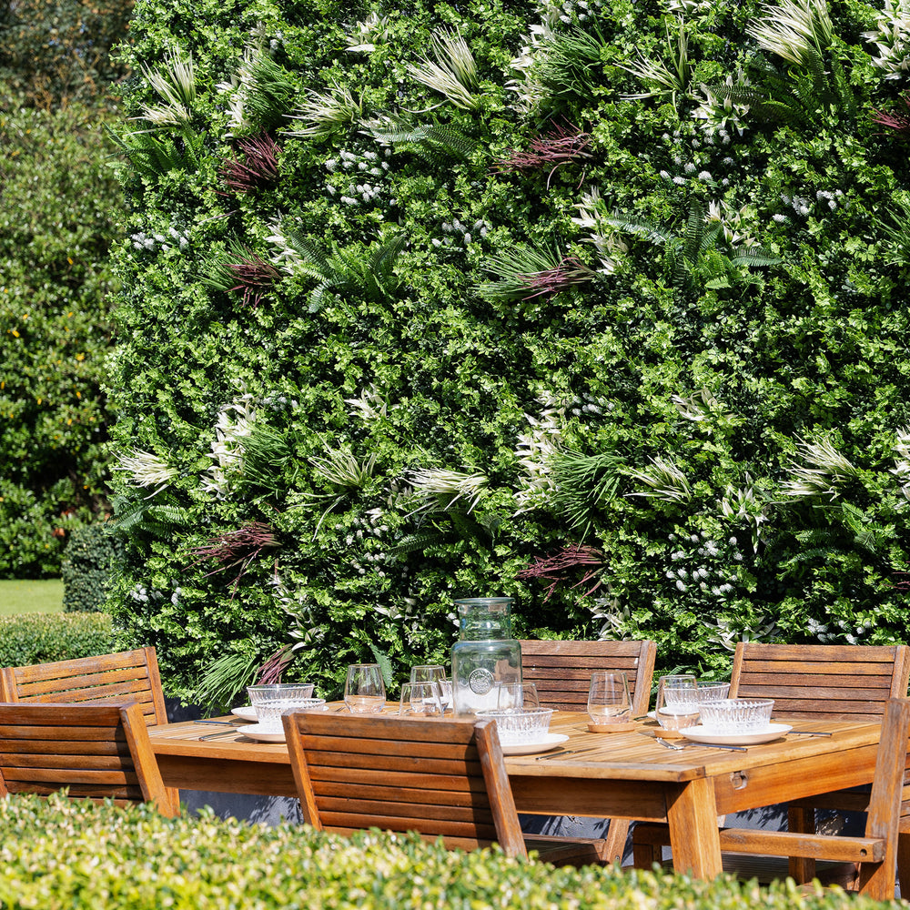 Wooden outdoor dining set with chairs against a lush green wall.