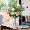 Floral arrangement in a vase on a coffee table with books and a couch in the background.