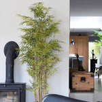 Tall artificial bamboo plant in a room with a black pipe and wooden trunk.