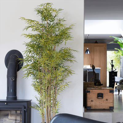 Tall artificial bamboo plant in a room with a black pipe and wooden trunk.